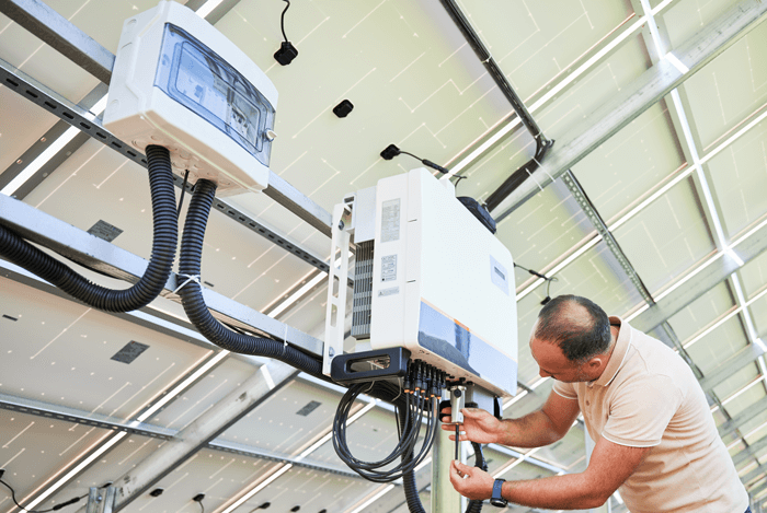 Dettaglio di un contatore bidirezionale installato vicino all'inverter per pannelli solari fotovoltaici, con tecnico qualificato che controlla